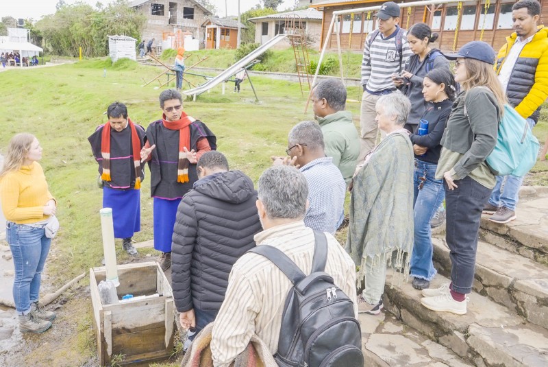 A member of the Misak community, wearing traditional dress, talks to a group of researchers gathered around him